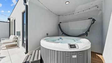 Un moderno espacio al aire libre con jacuzzi, banca y zona de estar cubierta.