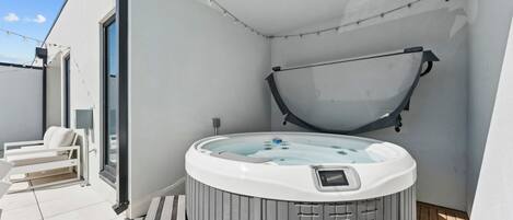 Un moderno espacio al aire libre con jacuzzi, banca y zona de estar cubierta.