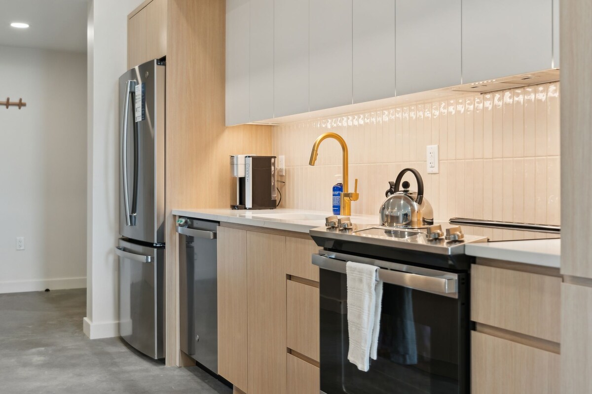 Eine moderne Küche mit Edelstahlgeräten, Holzschränken und einer schwarzen Arbeitsplatte.