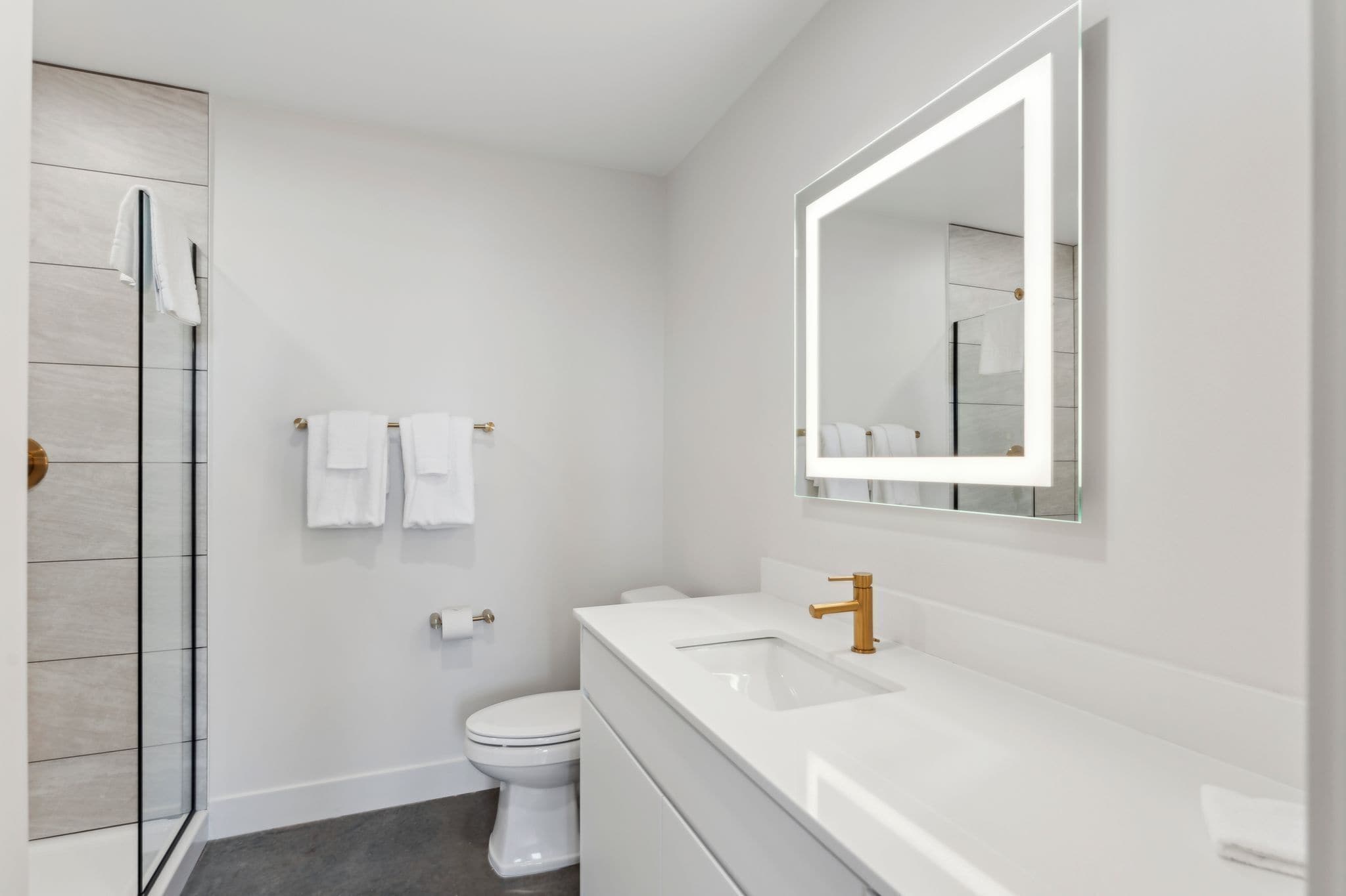 Un baño moderno con un lavabo blanco, un espejo grande y un box de ducha de vidrio.