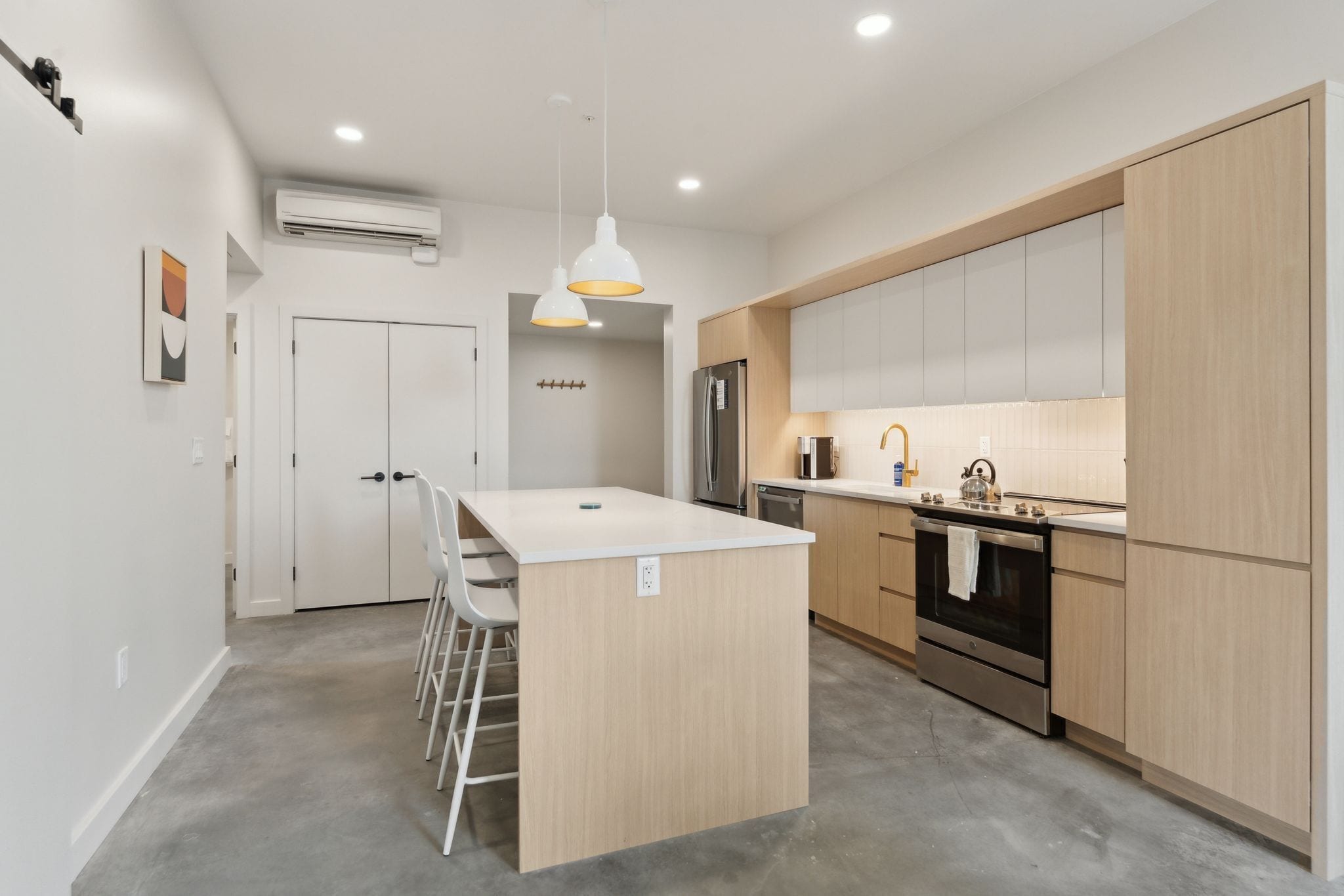 A modern kitchen with a central island, stainless steel appliances, and light wood cabinets.