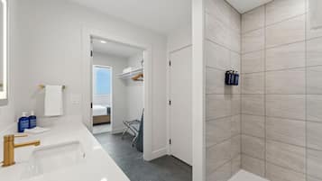 A modern bathroom with a white sink, gold faucet, and a shower area with beige tiles.