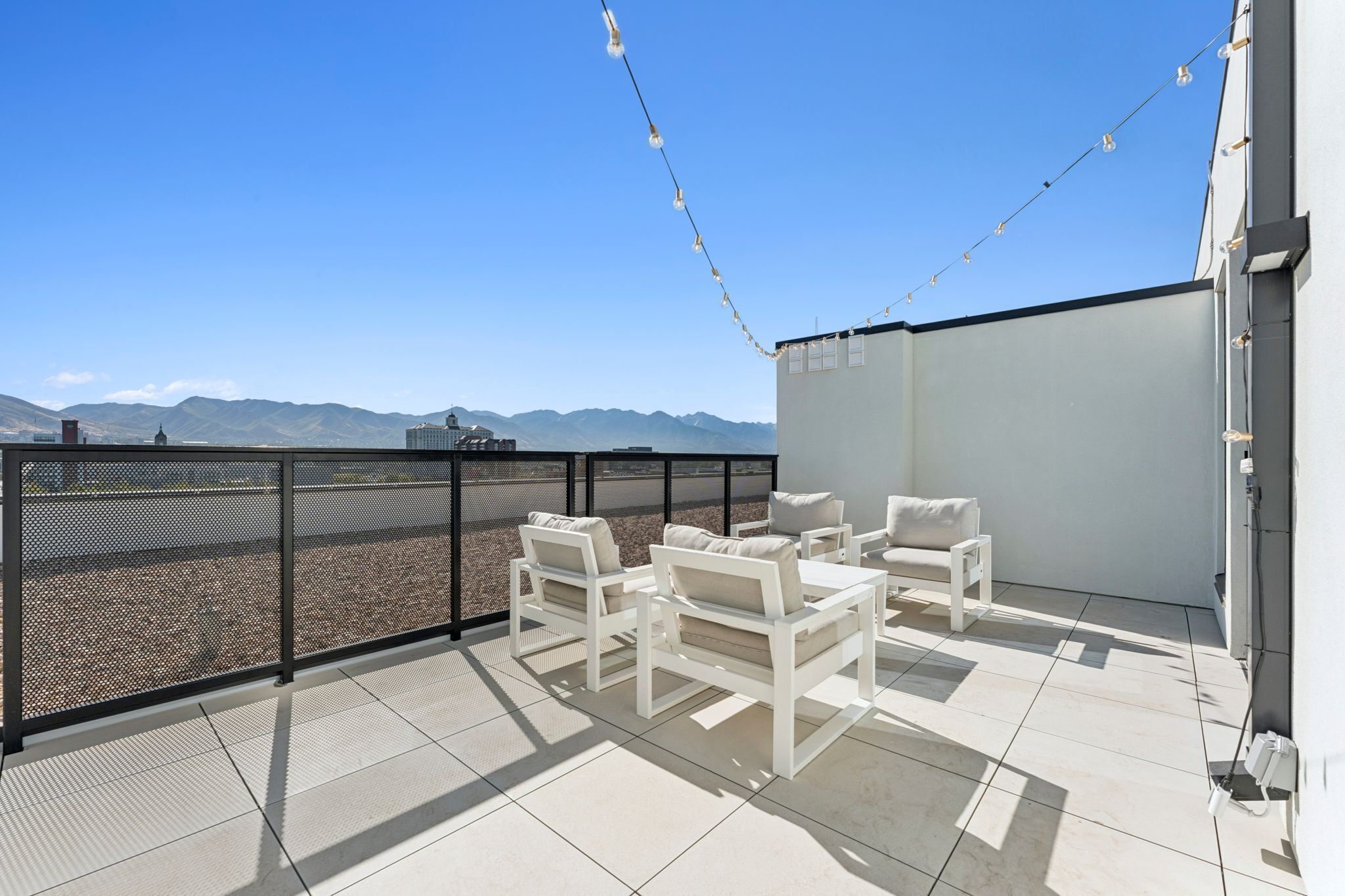 Una terrazza sul tetto con mobili bianchi, vista sulle montagne e luci decorative.