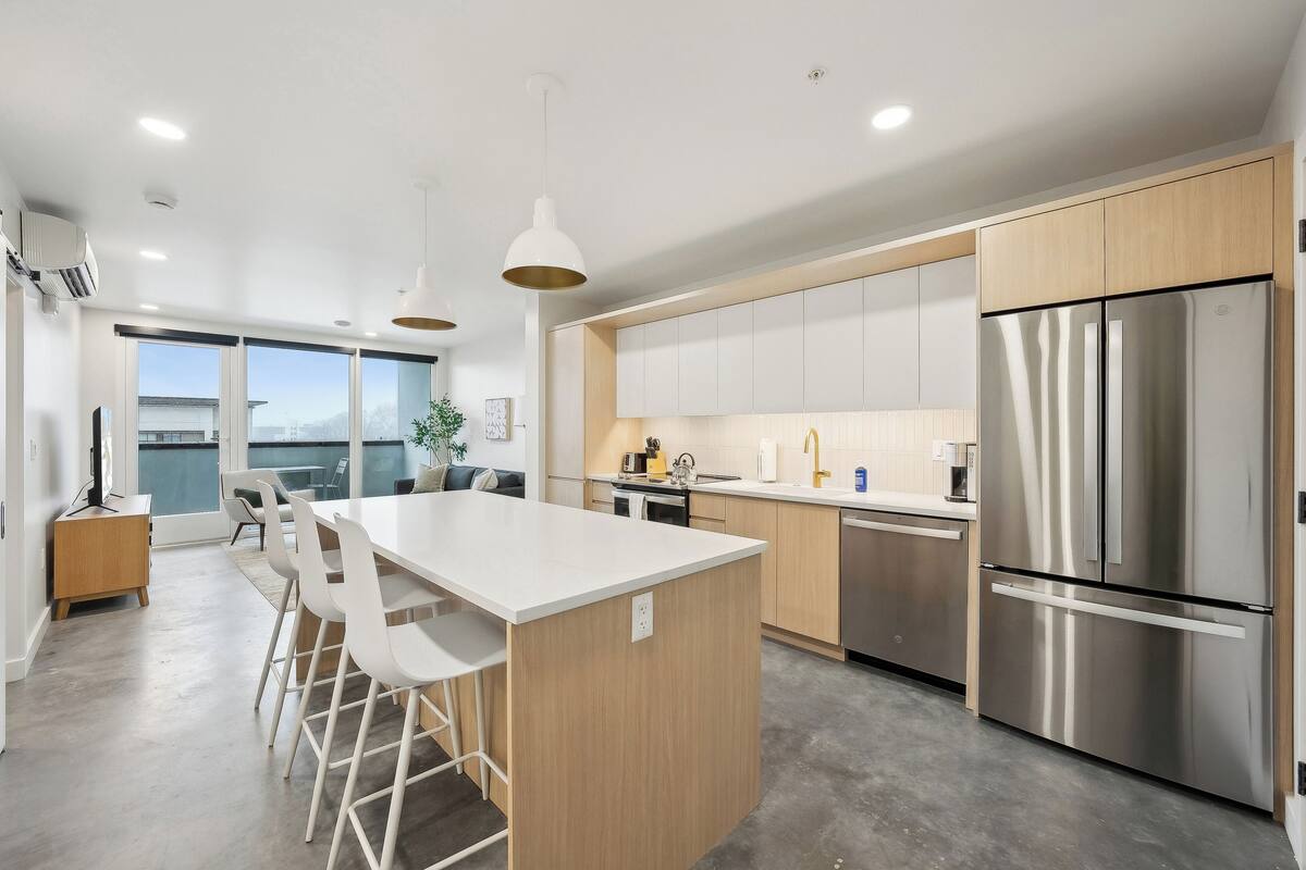 A modern kitchen with a central island, stainless steel appliances, and a view to the outside.
