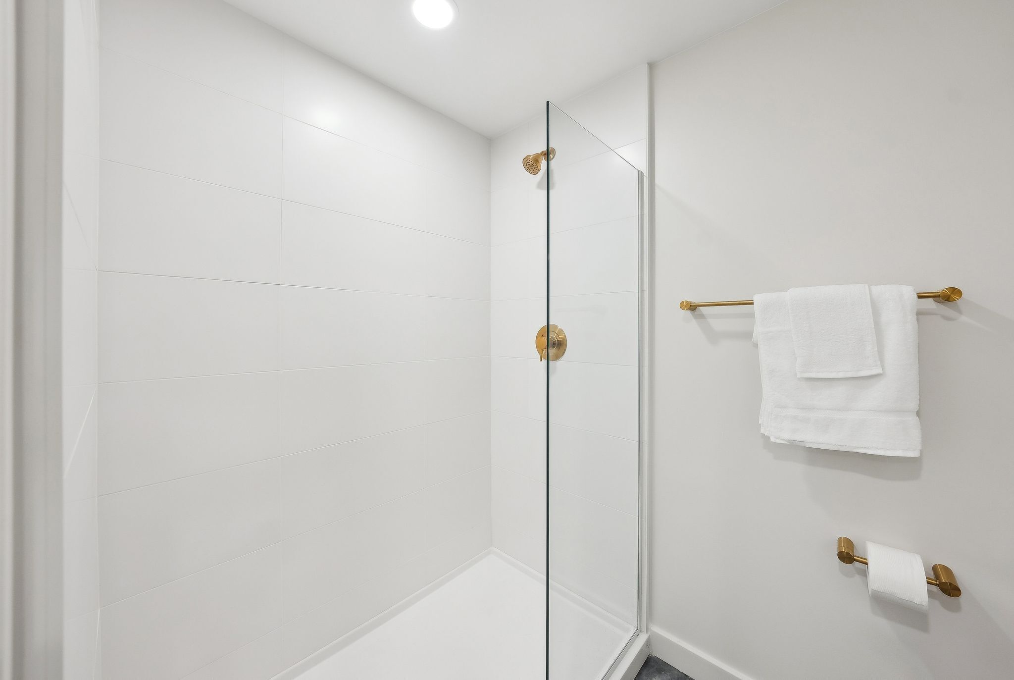 A modern bathroom with white tiles, a glass shower enclosure, and gold fixtures.