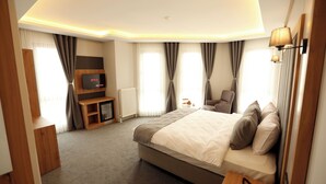 A modern hotel room with a large bed, a TV, a wooden side table, and a lamp. - KARAKOÇ HOTEL  (Van)