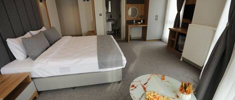 Una habitación de hotel moderna con una cama grande, un escritorio pequeño, una mesa redonda con un plato de comida y un armario.