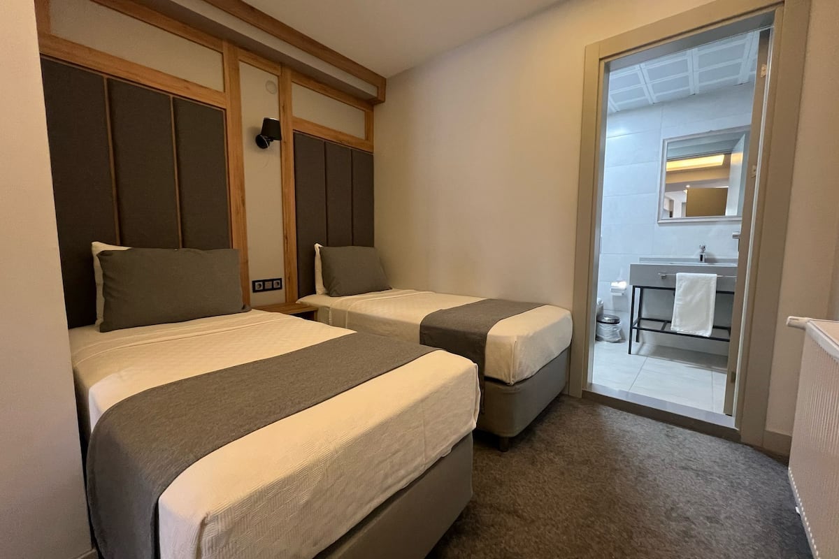 A hotel room with two beds, a small bathroom with a sink, and a view of the outside through a glass door.