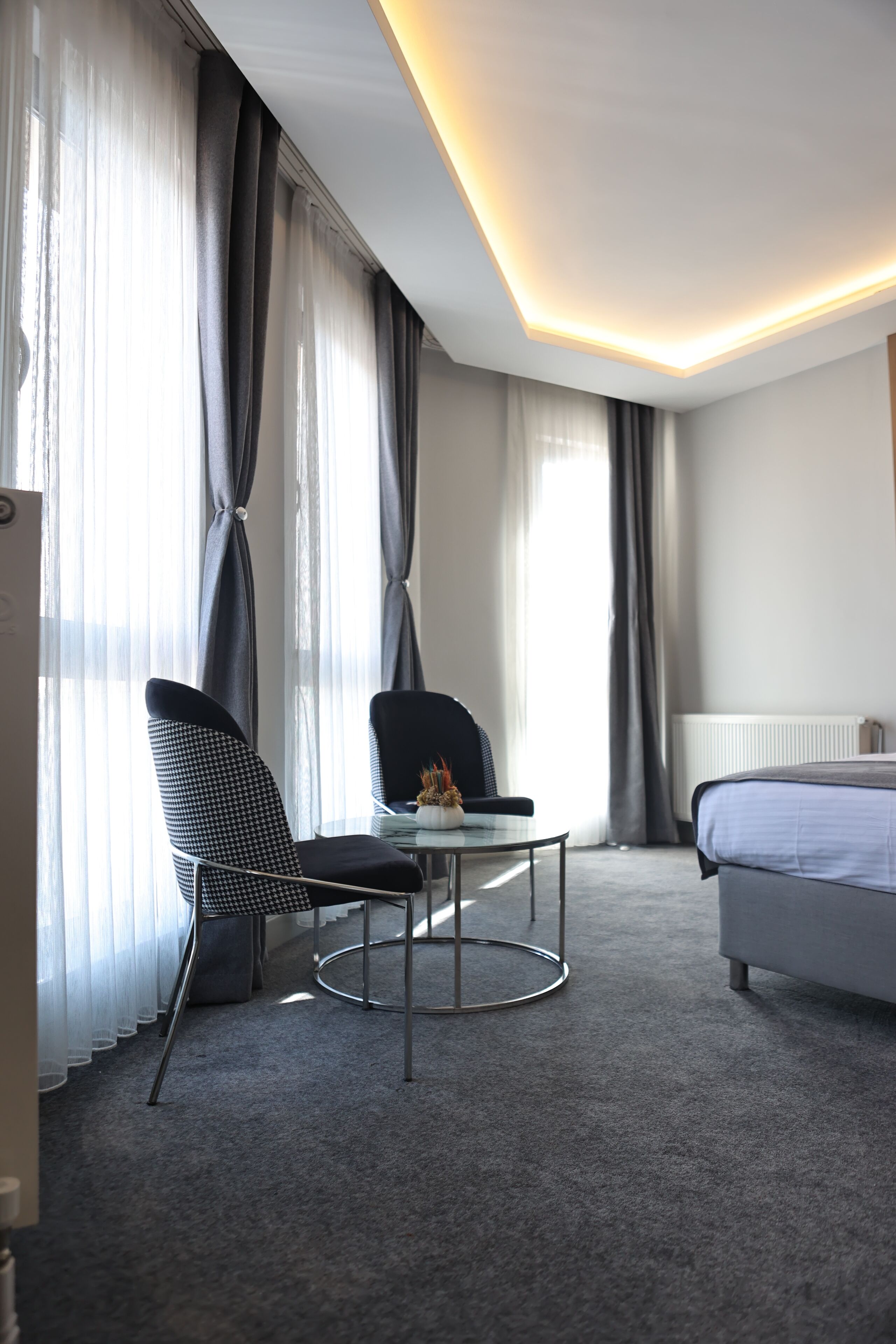 Una habitación de hotel con una cama, una silla, una mesita y una ventana con cortinas.