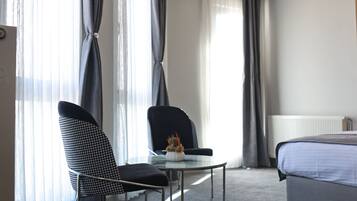 A hotel room with a bed, a chair, a small table, and a window with curtains.