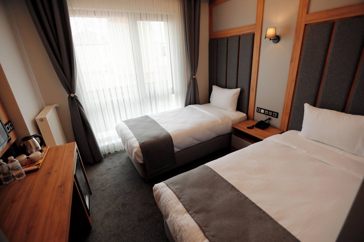 A hotel room with two beds, a wooden desk with a kettle, and a nightstand with a lamp.