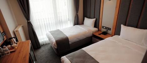 Habitación de hotel con dos camas, un escritorio de madera con hervidor y una mesita de noche con lámpara.