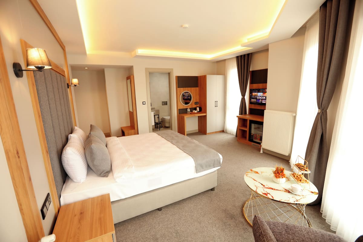 A modern hotel room with a large bed, a small table, a TV, and a bookshelf.