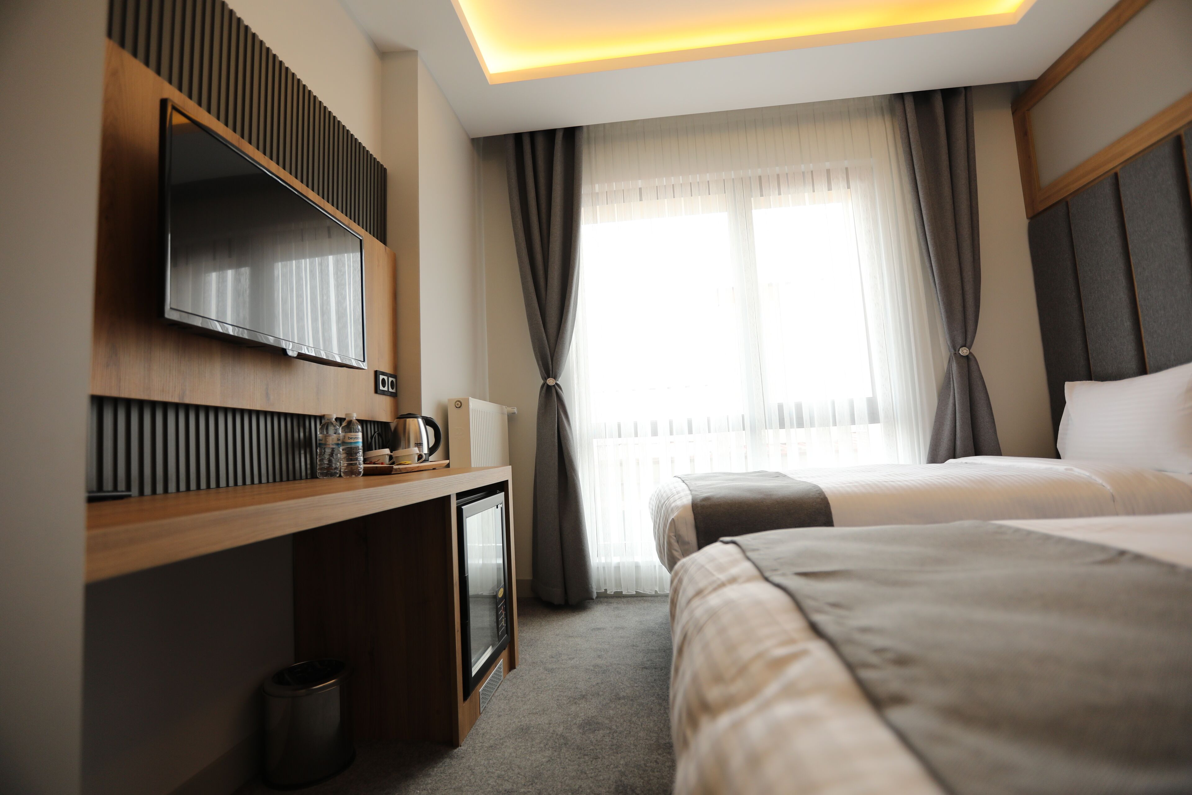 Une chambre d’hôtel avec un lit, un bureau avec une télévision, une machine à café et une fenêtre avec des rideaux.