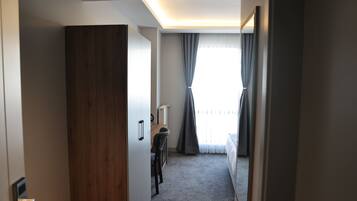 A hotel room with a wooden wardrobe, a desk with a chair, a bed, and a window with curtains.