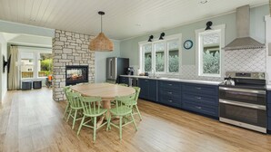 A modern kitchen with a stone wall, wooden dining table, green chairs, and stainless steel appliances. - "BRAND NEW"  Littoral Lookout at Pacific Beach (Pacific Beach)