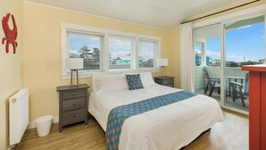 A bedroom with a bed, two bedside tables, a radiator, a window with blinds, and a balcony with chairs. - "BRAND NEW"  Littoral Lookout at Pacific Beach (Pacific Beach)