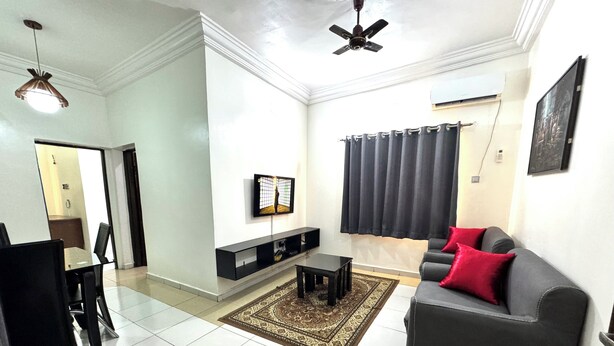 A living room with a grey sofa, black armchairs, a coffee table, and a TV on a black stand. There is a patterned rug on the floor and a ceiling fan above. - 1BEDROOM FLAT at UTAKO ABUJA. 24hrs LIGHT, WIFI & KITCHEN (Abuja)