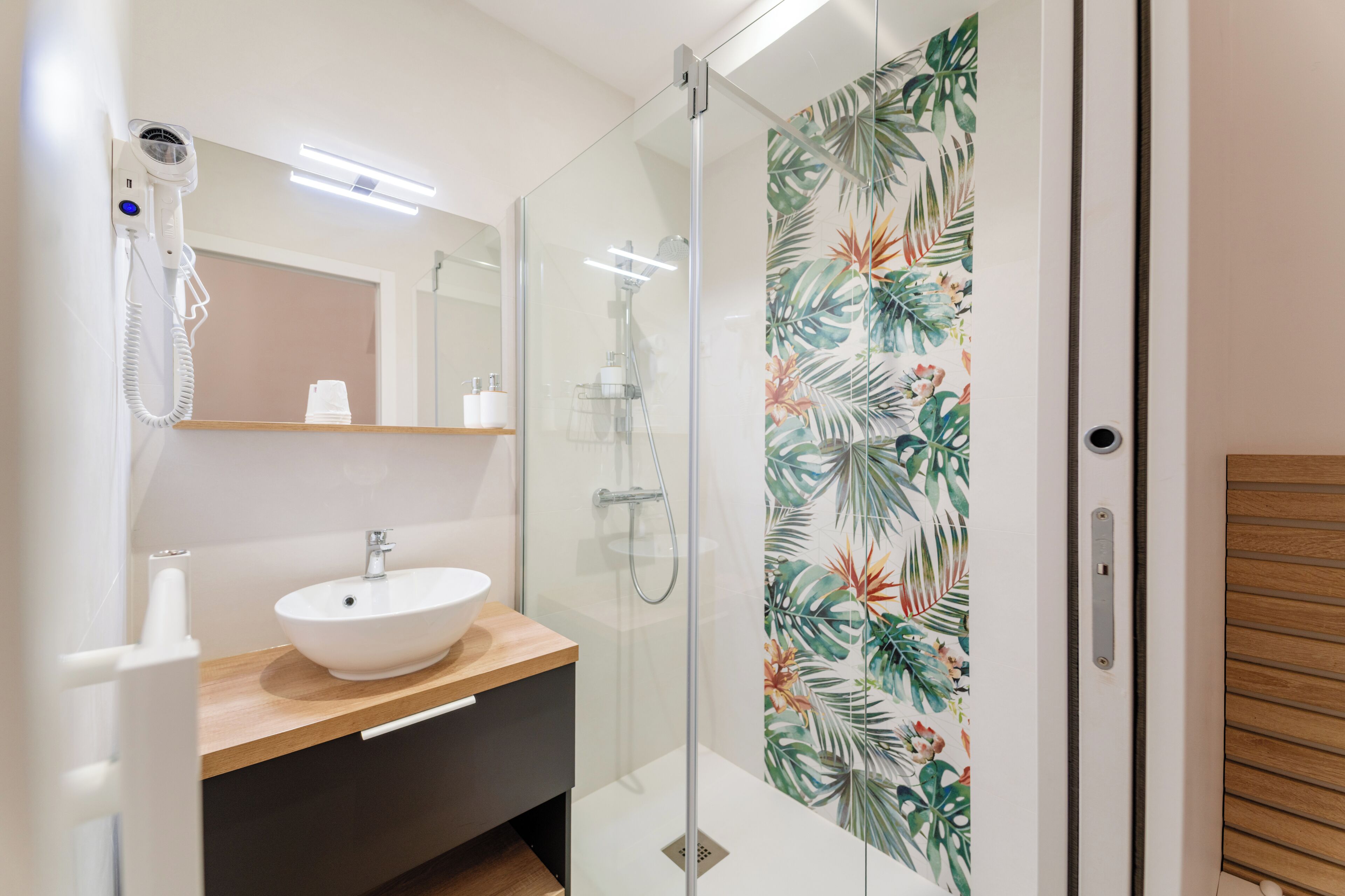 Ein modernes Badezimmer mit Duschkabine aus Glas, einem weißen Waschbecken und einem an der Wand befestigten Föhn.