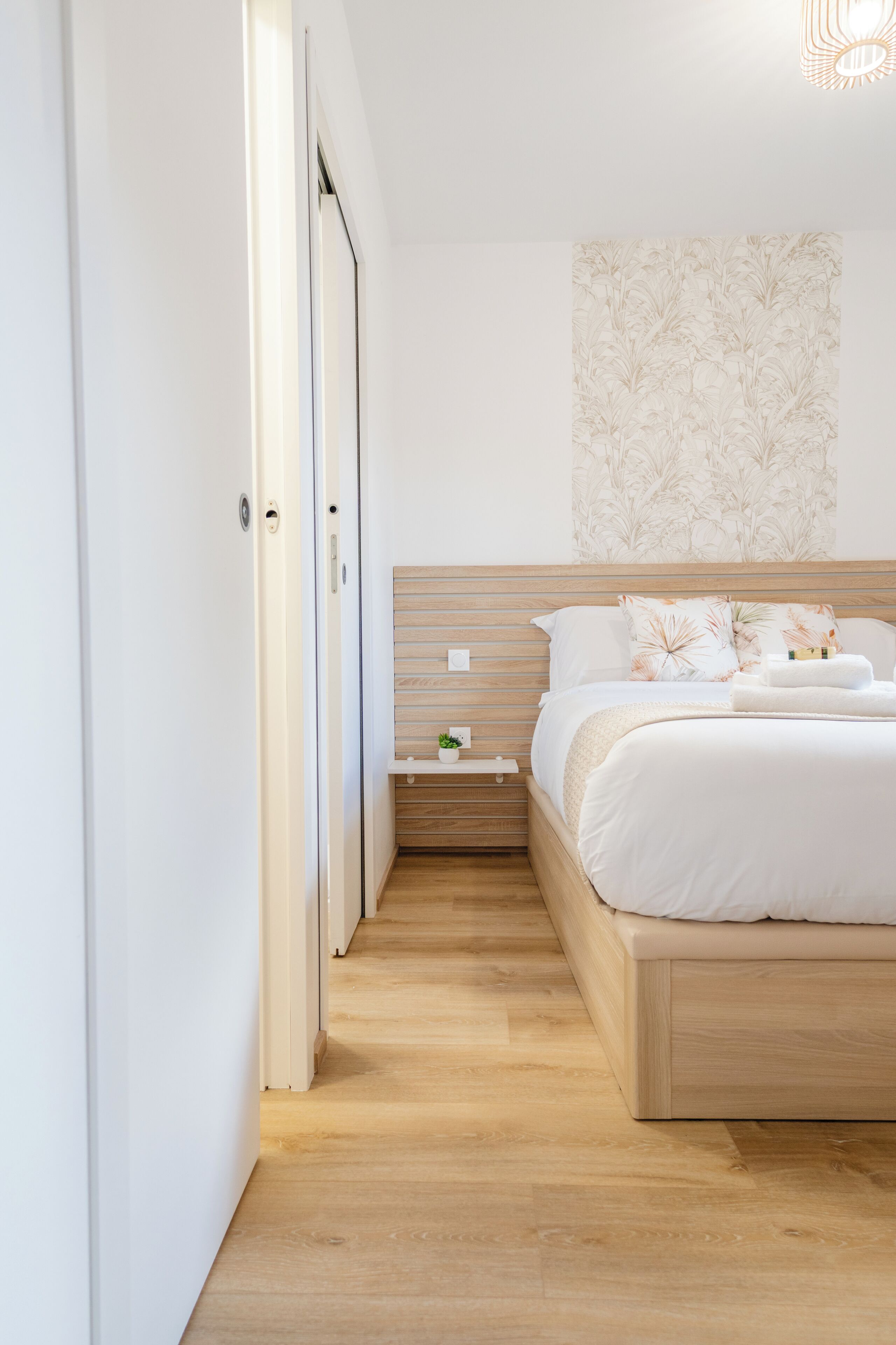 Ein Schlafzimmer mit einem hölzernen Kopfende, einem Nachttisch mit Pflanze und einer Wand mit floralem Muster.