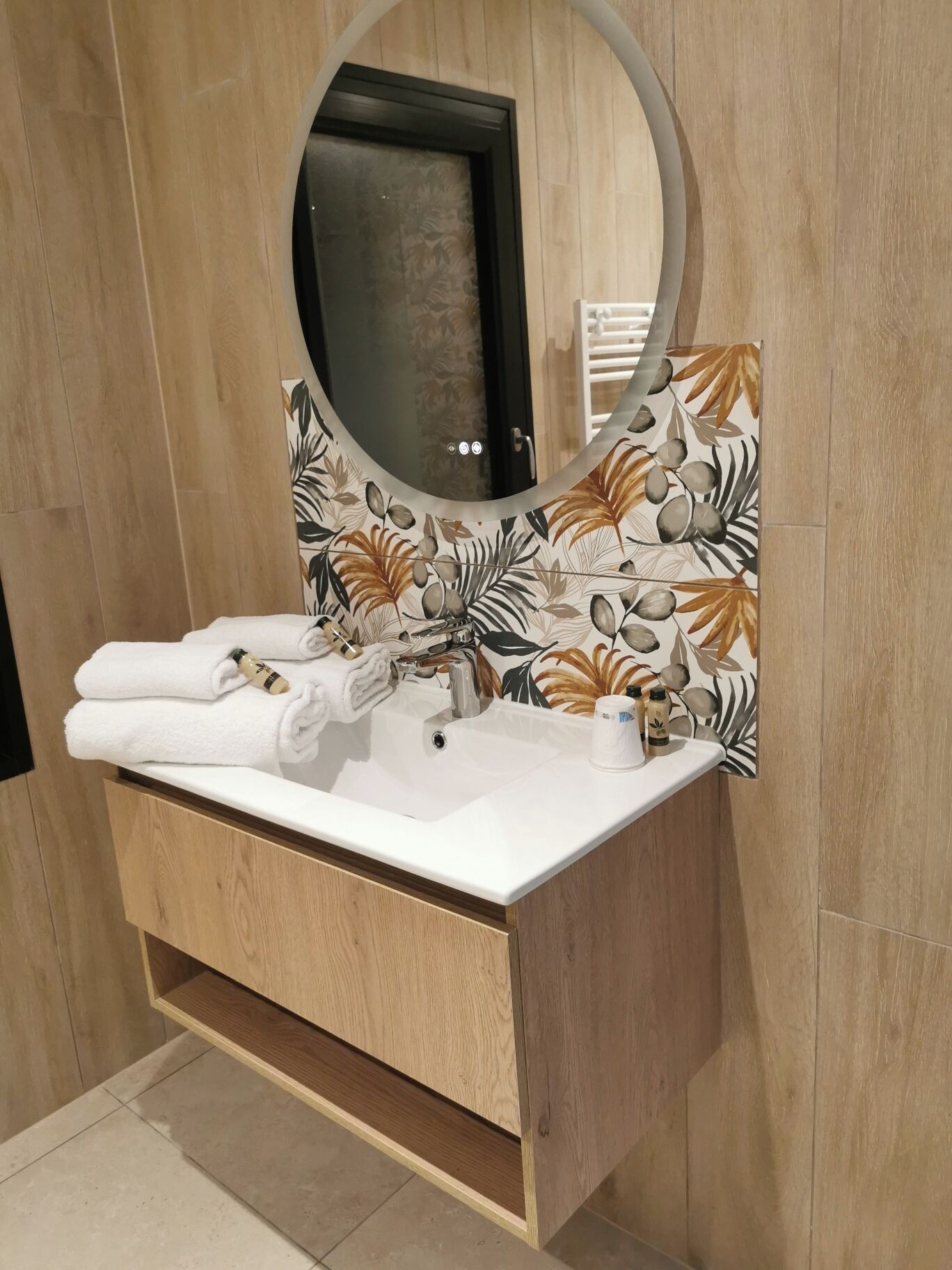 A bathroom with a wooden vanity, a round mirror, and a sink with two towels.