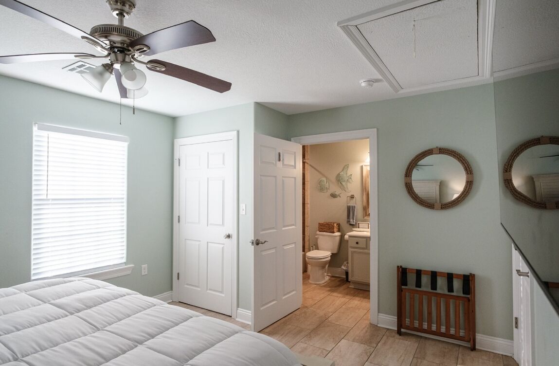 Un dormitorio con cama, ventilador de techo y puerta que da a un baño.