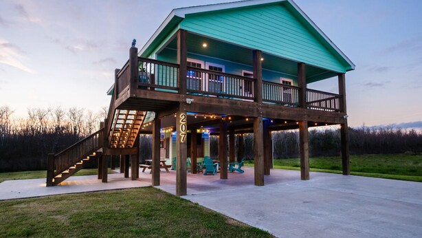 A two-story wooden cabin with a balcony, numbered 207, featuring a covered patio area with outdoor seating and string lights. - Angler’s Paradise! Amazing fishing w/ in minutes! 3 bed,sleeps 7 ppl, 2 bath. (Hackberry)