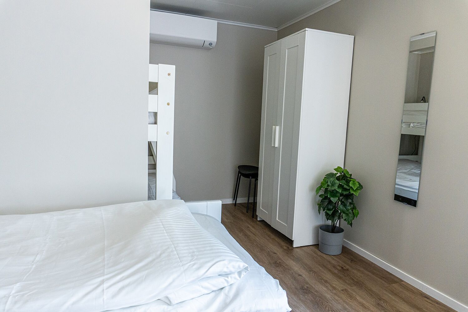 A bedroom with a bed, a wardrobe, a small stool, and a potted plant.