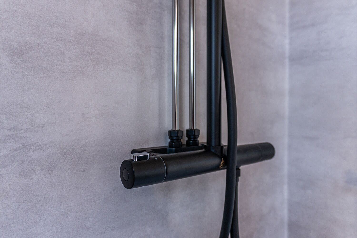 A shower head attached to a wall with a control knob and two hoses.