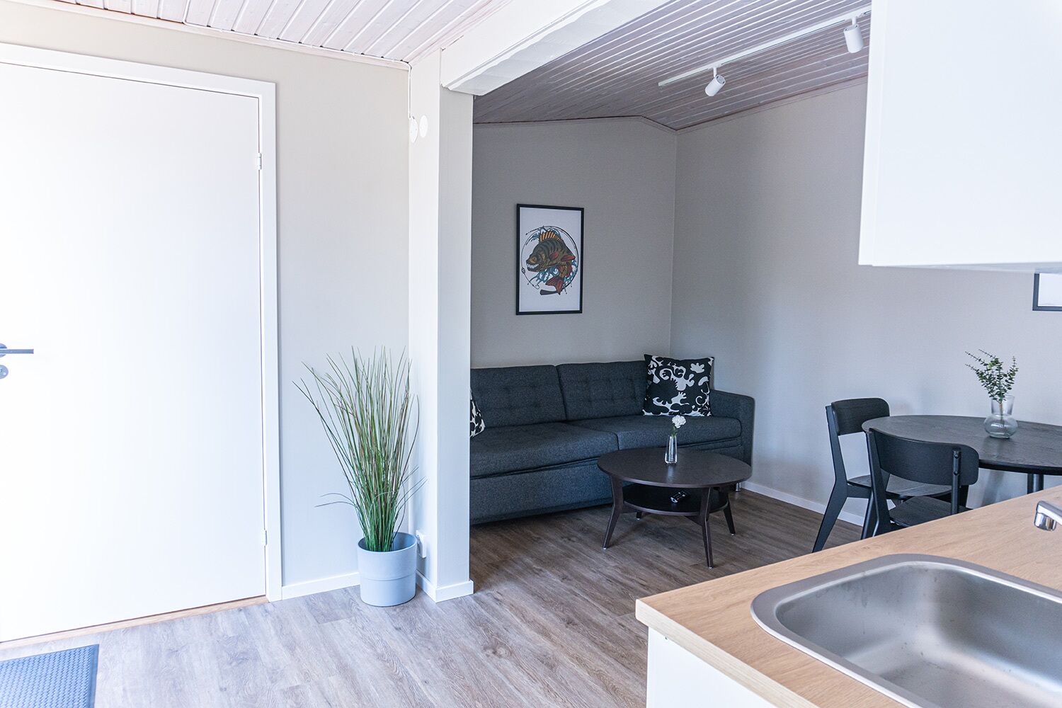 A modern living room with a grey sofa, a small round table, and a dining area with a dark table and chairs.