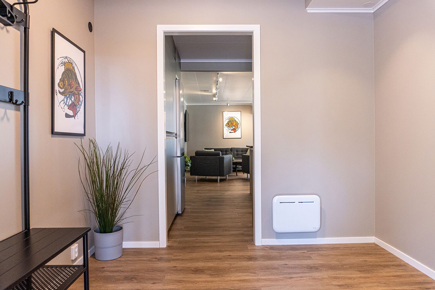 A hallway with a wooden floor, a potted plant, and framed artwork on the wall.