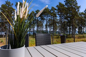 A deck with outdoor furniture, a potted plant, and a view of a forest and lake. - Perchlodge (Monsteras)