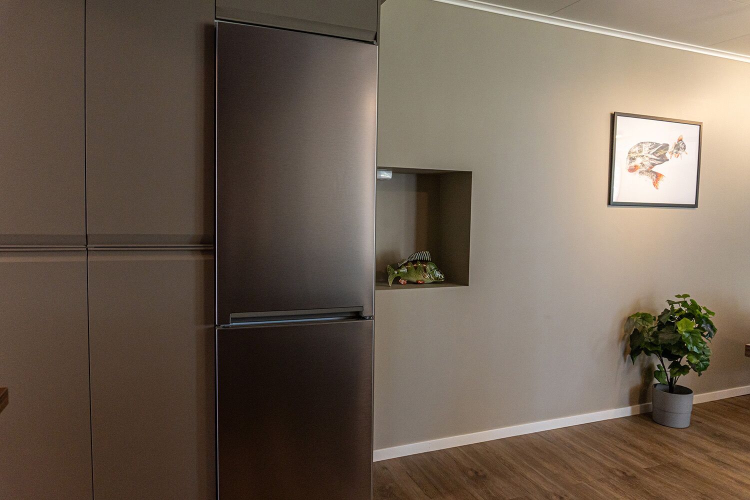 A modern kitchen with a stainless steel refrigerator, a small fish decoration, and a potted plant.
