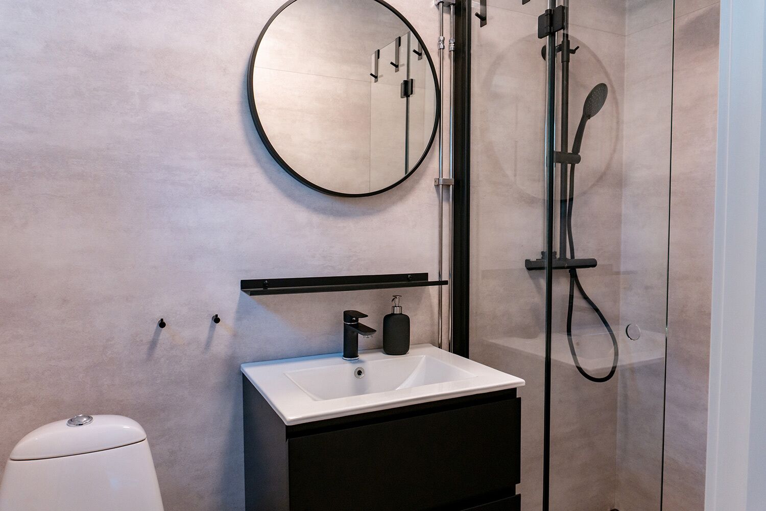 A modern bathroom with a round mirror, a white sink, and a black cabinet.
