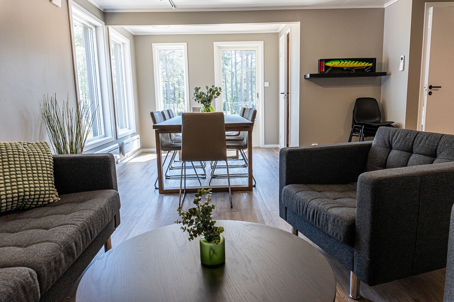 A living room with a dark brown sofa, a round coffee table with a green vase, and a dining area with a wooden table and chairs.