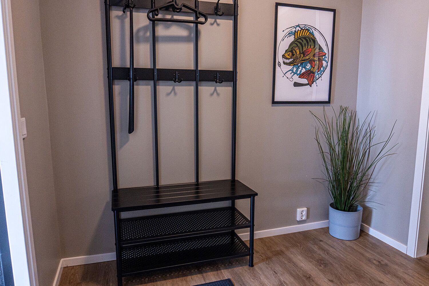 A hallway with a black metal bench, a wall-mounted coat rack, and a framed fish illustration.