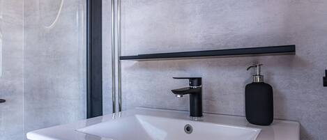 A modern bathroom with a white sink, black faucet, and soap dispenser.