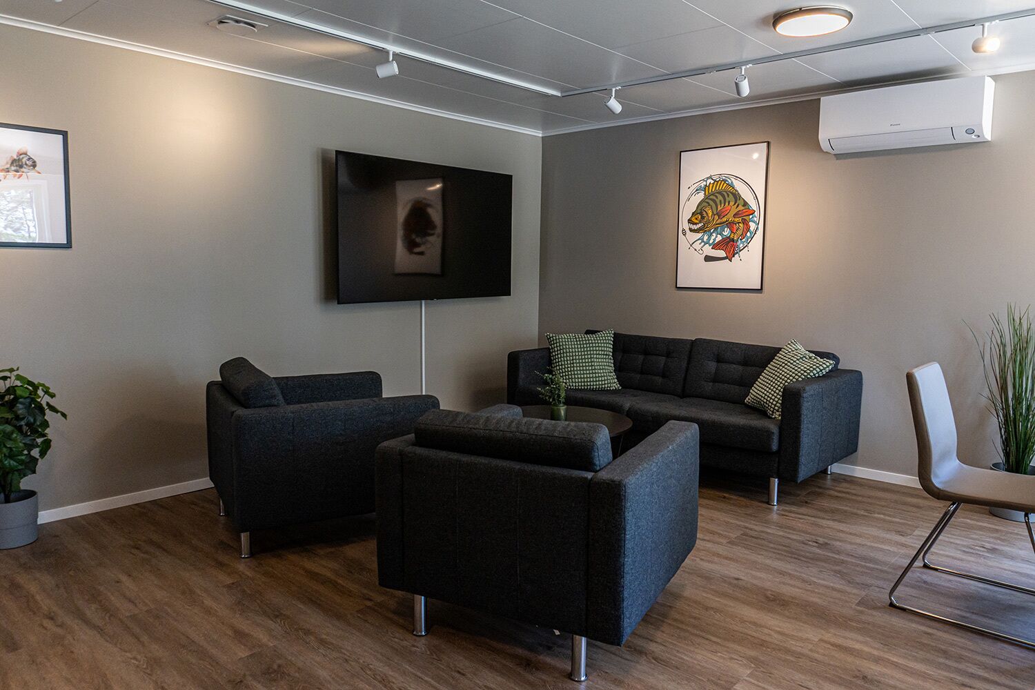 A modern living room with a grey sofa set, a flat-screen TV mounted on the wall, and a framed artwork above the sofa.