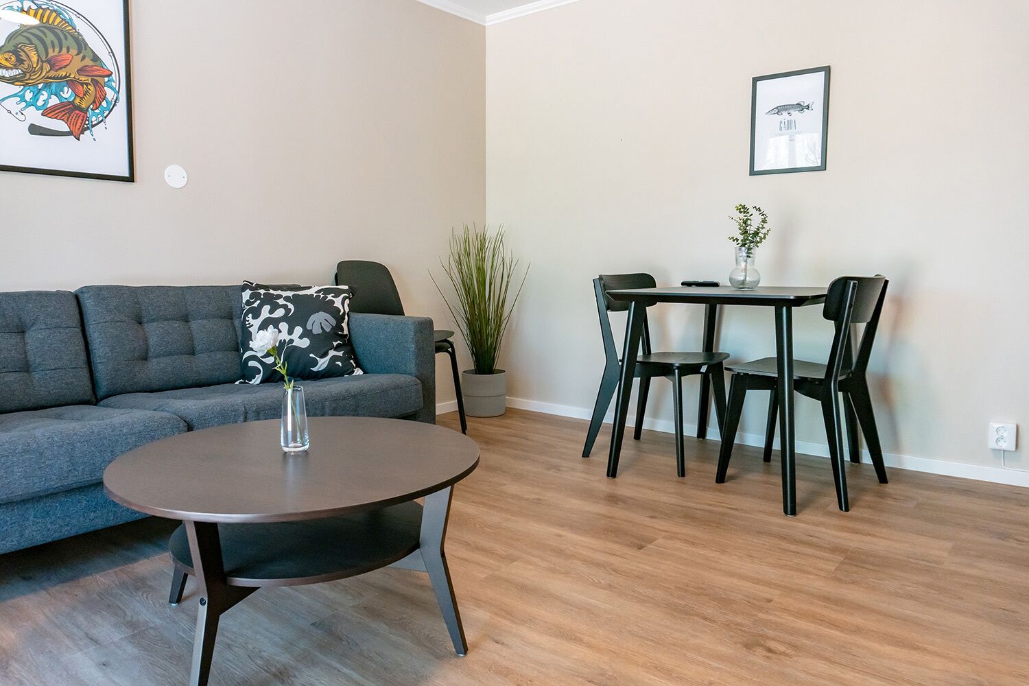 A modern living room with a grey sofa, a round coffee table, and a dining area with a table and chairs.