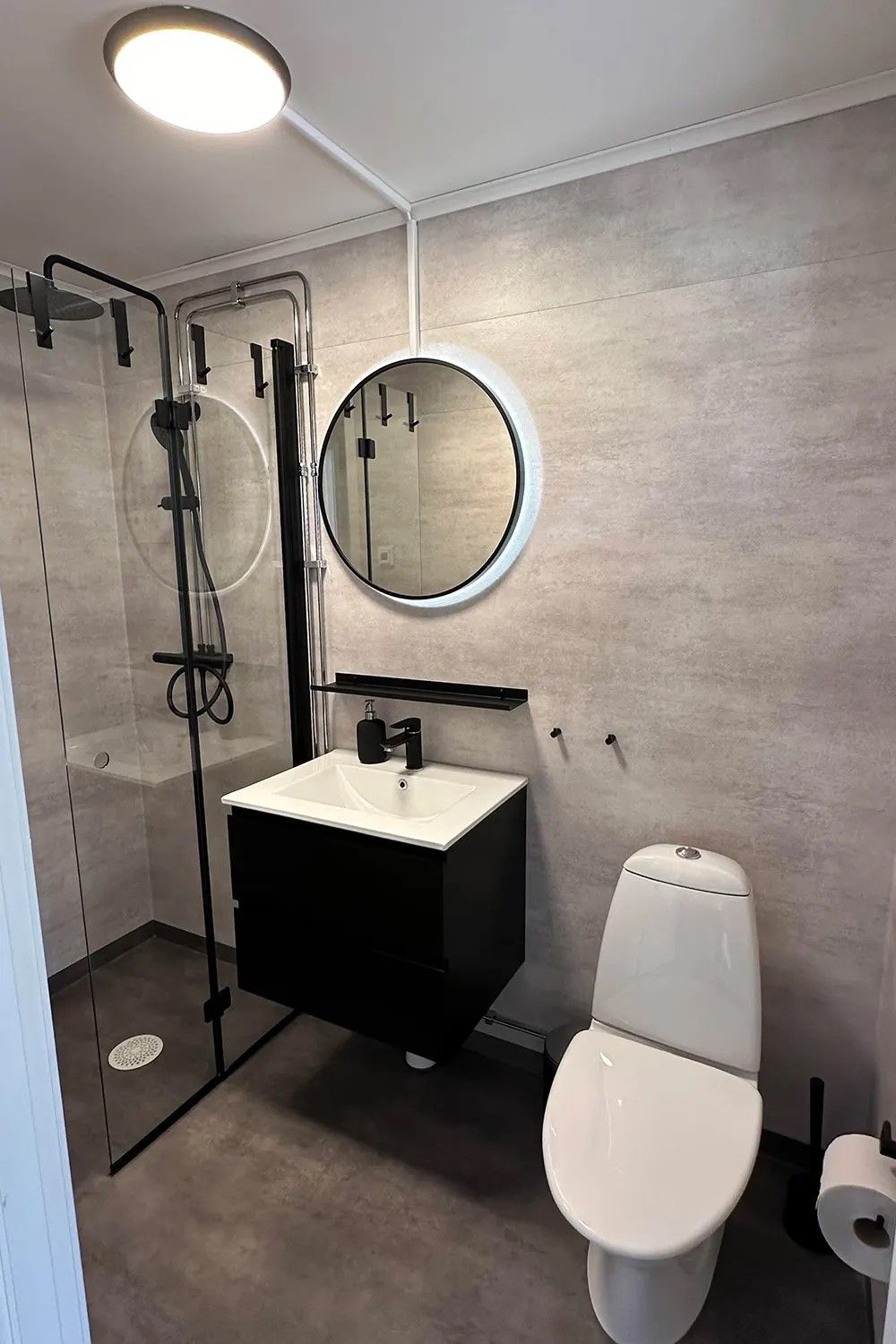 A modern bathroom with a glass-enclosed shower, a white sink, a toilet, and a round mirror.