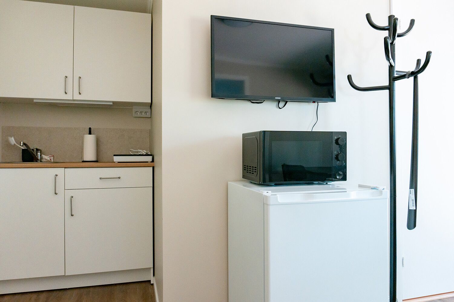 A compact kitchen with white cabinets, a microwave on a white appliance, and a TV mounted on the wall.