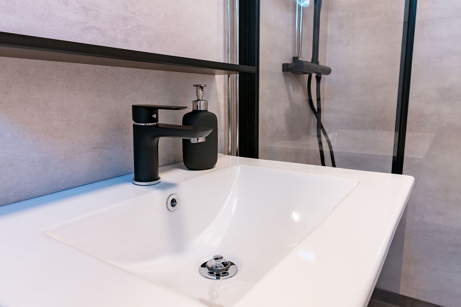 A modern bathroom with a white sink, black faucet, and a glass shower enclosure.