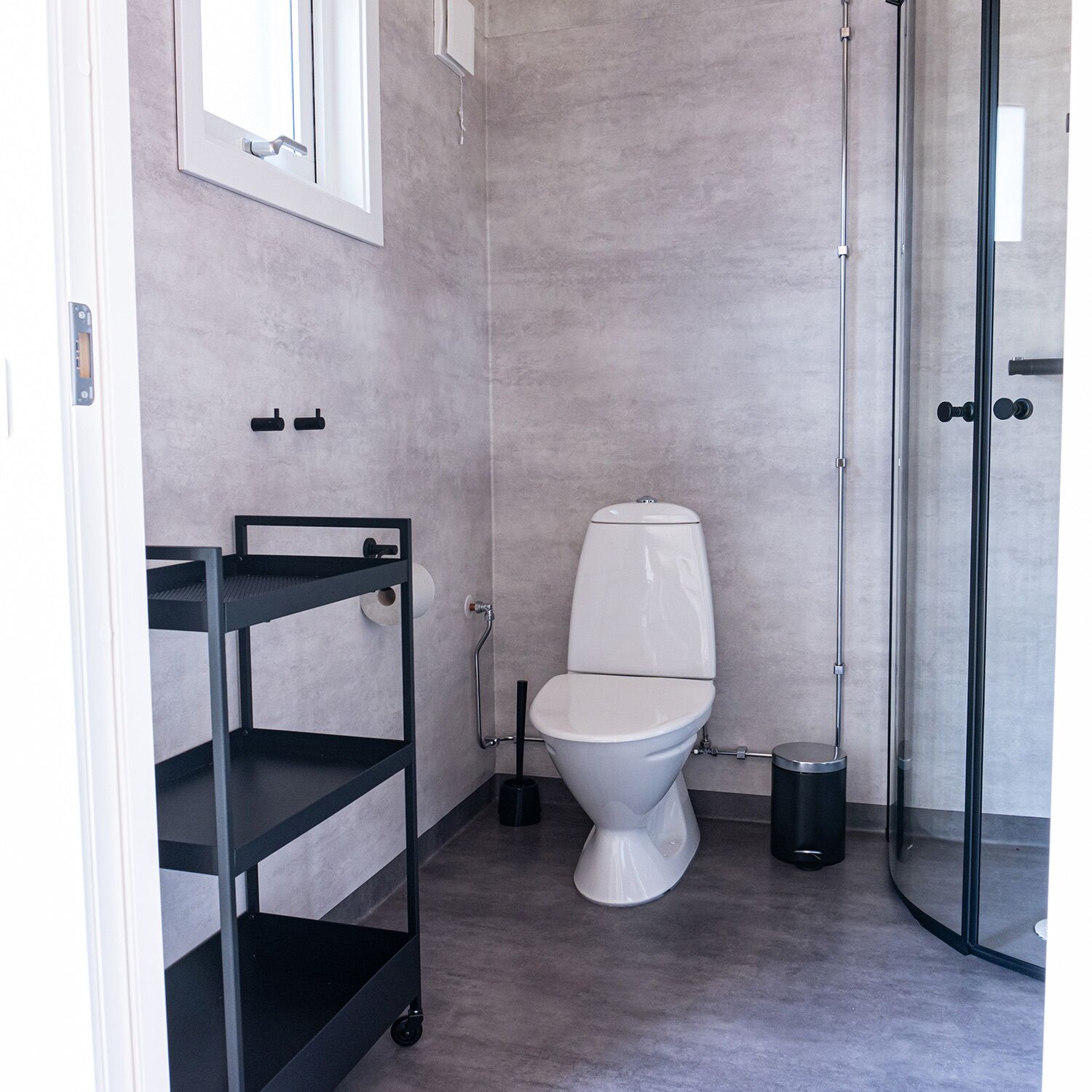 A modern bathroom with a toilet, a shower, and a black metal cart.