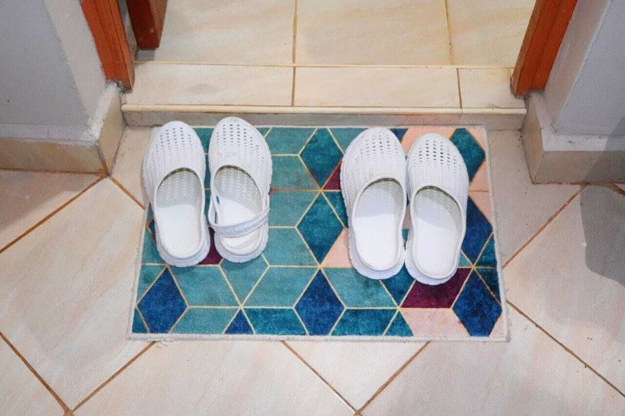 A pair of white slippers on a colorful tiled mat at a doorway.