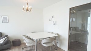 A modern, well-lit room with a white table and chairs, a grey sofa, and a glass partition. - Apartment in Middelkerke With Sea Views (Middelkerke)