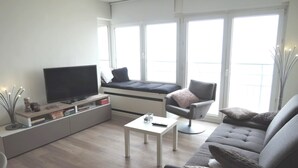 A modern living room with a flat-screen TV, a sofa, a chair, and a small coffee table. - Apartment in Middelkerke With Sea Views (Middelkerke)