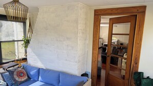 Un salon avec un canapé bleu, une porte en bois et une cuisine visible à travers une porte ouverte.