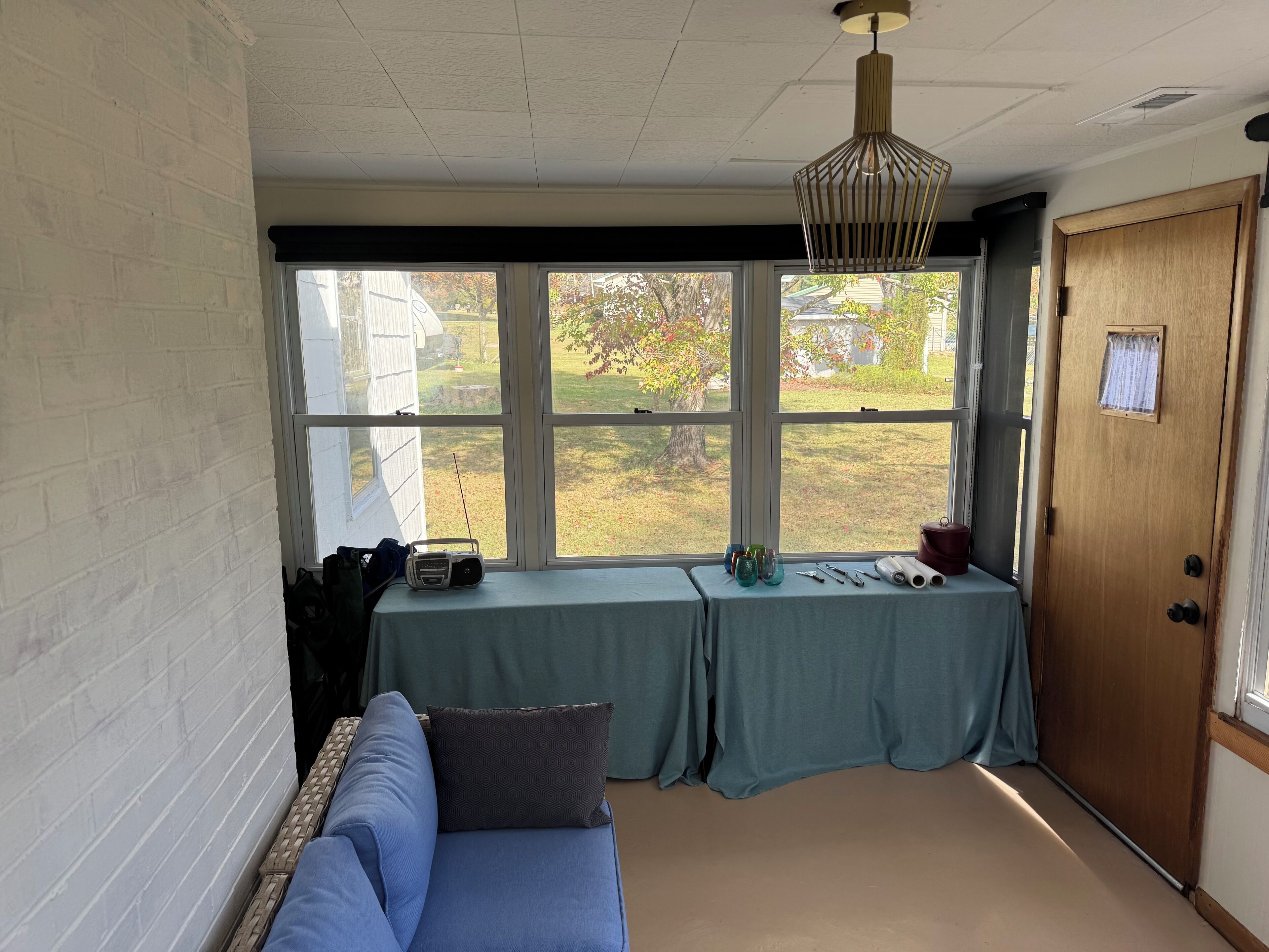 A room with a blue sofa, a table with various items, and a view of a yard through large windows.