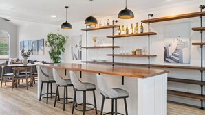 Una cocina moderna con una isla central, taburetes de bar, iluminación colgante y estanterías abiertas con botellas y copas.