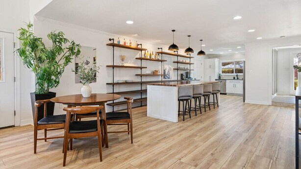 Una cocina moderna con suelo de madera, una isla central con taburetes de bar y estanterías empotradas con utensilios de cocina.
